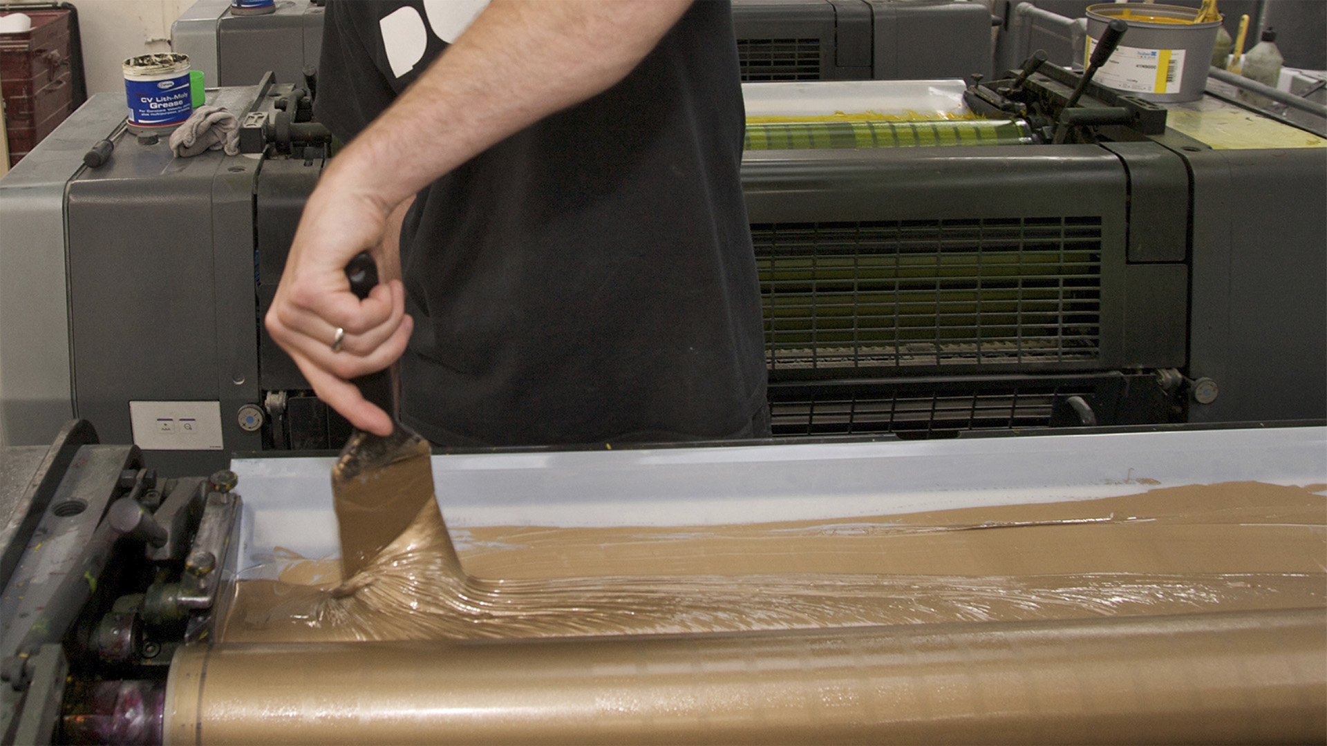 A person mixing paint inside a print tray for the gold print process for the Mintel Loop Book