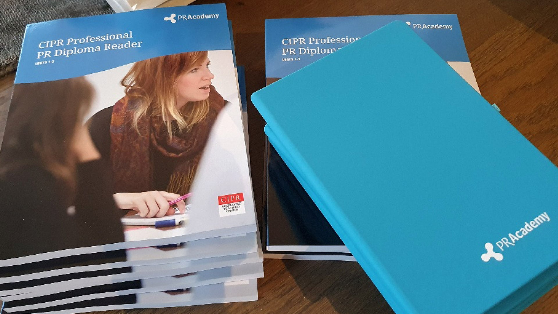 A photograph of a stack of blue PR Academy CIPR Professional PR Diploma Reader brochures and notebooks